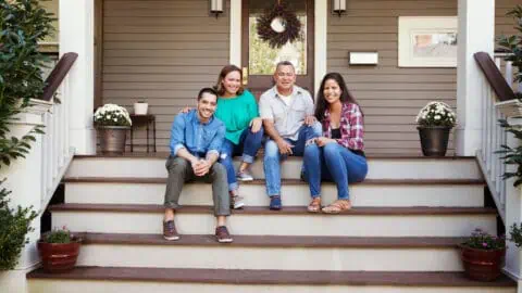 parents and their college-age children sit on the porch of a home in a college town