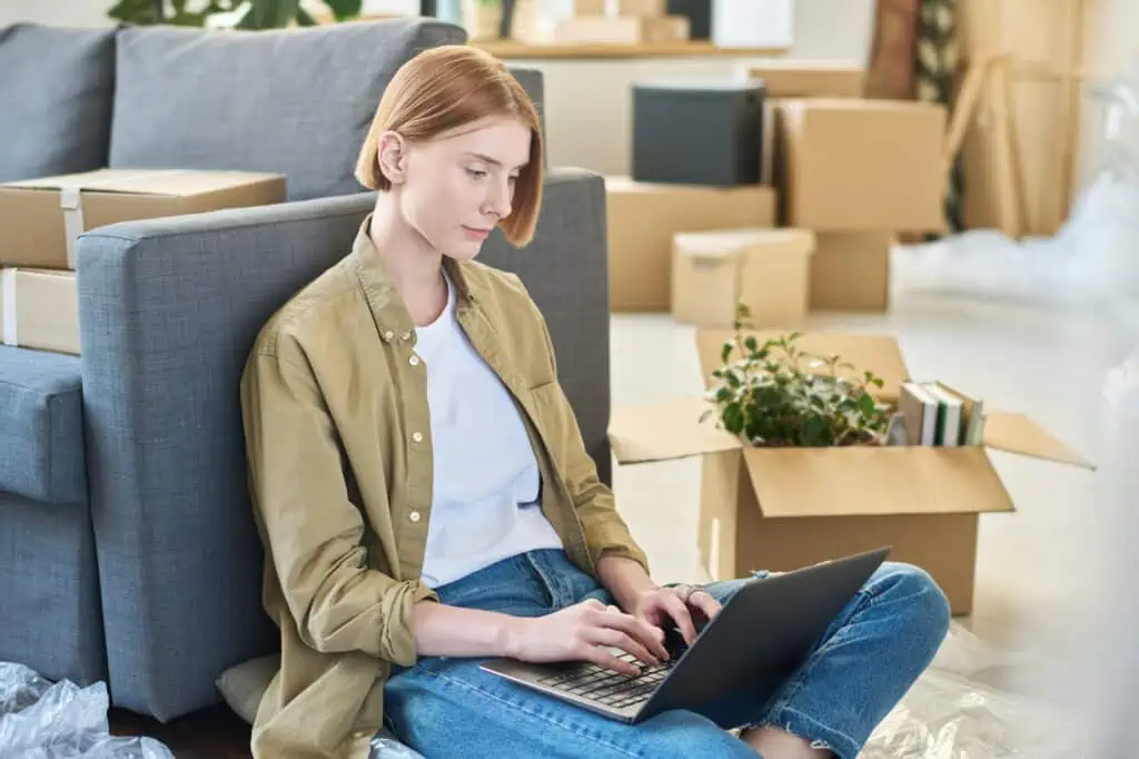 a woman looks at a laptop while surrounded by moving boxes