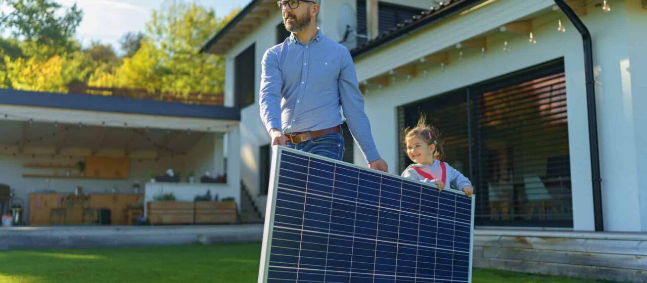 a father and daughter move a solar panel by carrying it across a lawn