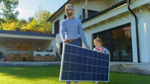 a father and daughter move a solar panel by carrying it across a lawn