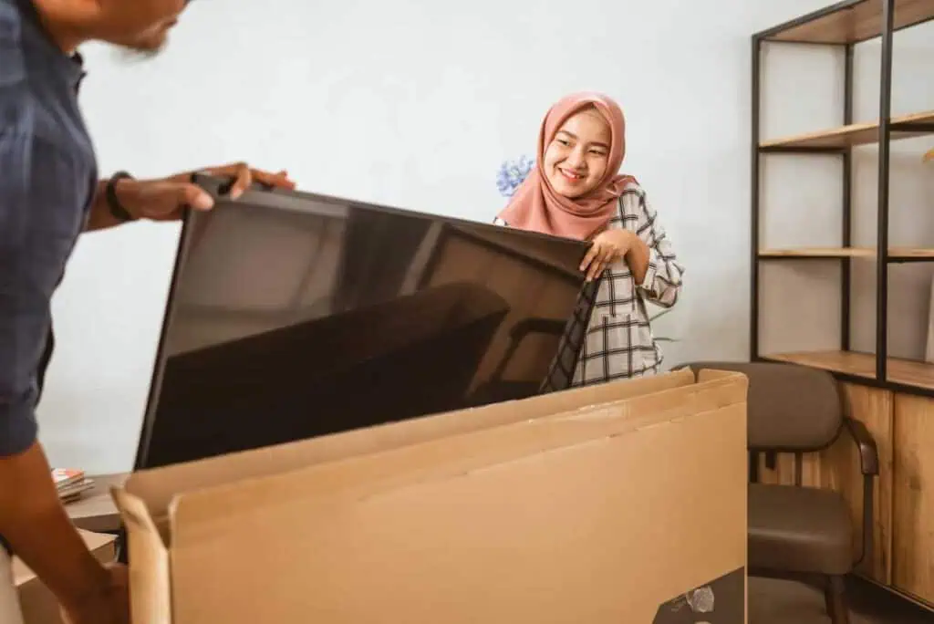 a woman and another person off-screen readies a tv to put it in a box