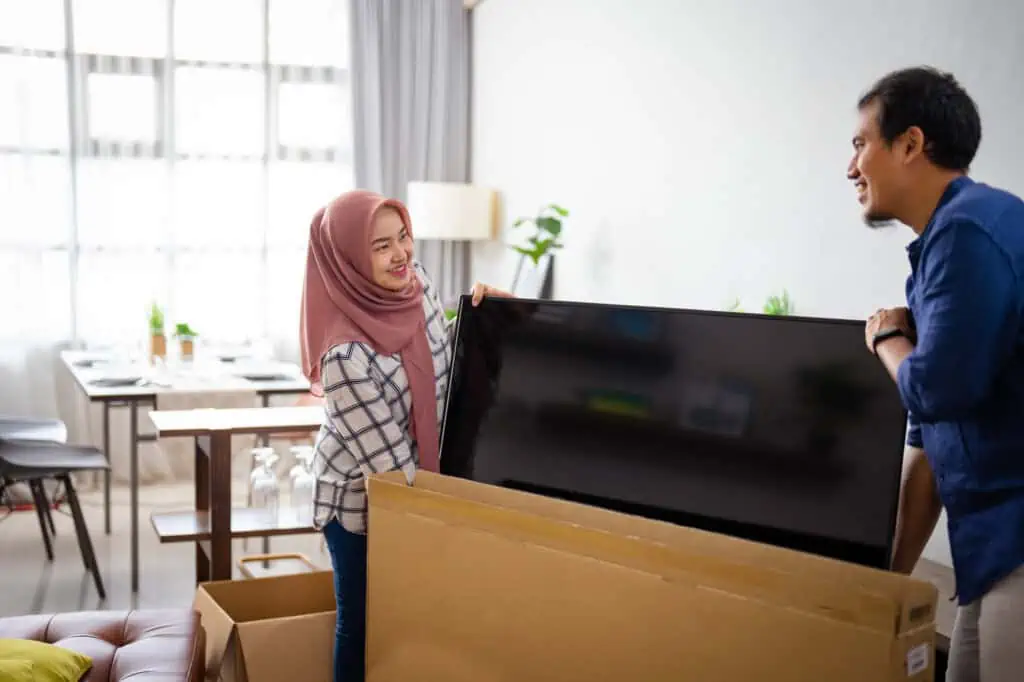 a couple prepares to pack a flatscreen tv into a box