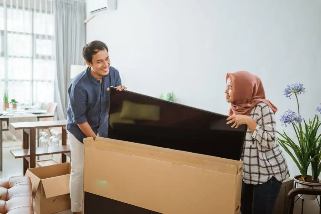 A couple hold onto a flat screen tv next to its box