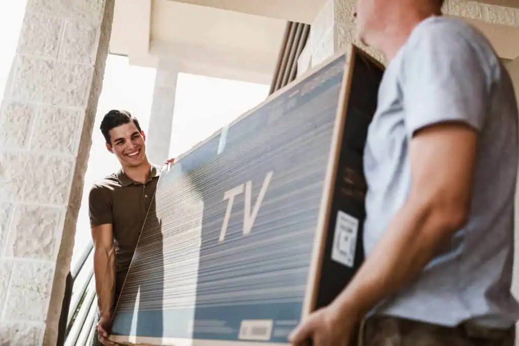 two men carry a flatscreen tv through a doorway