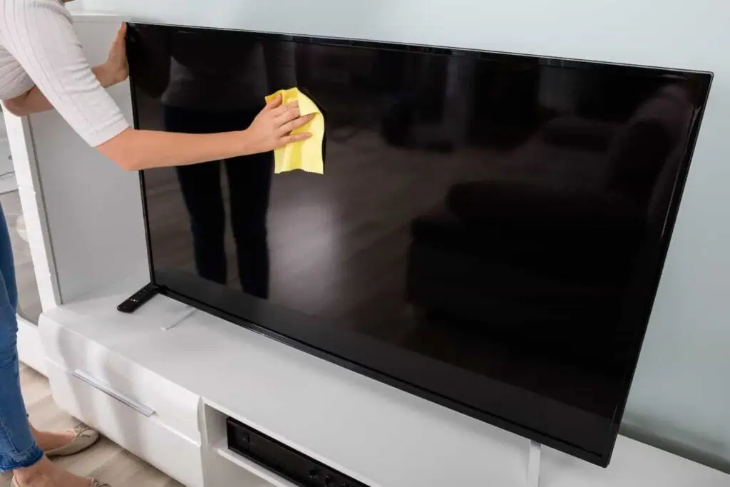A person cleans the screen of a large flatscreen tv with a yellow microfiber cloth