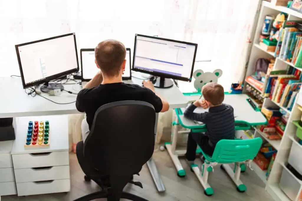 a man sits in his home office with his child sitting next to him at their own more colorful desk