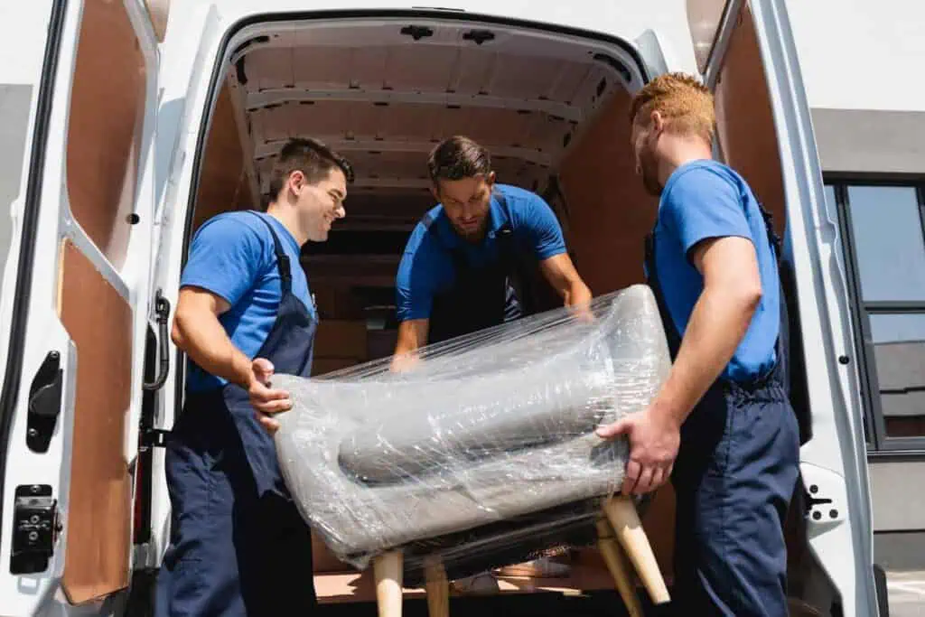 Three workers load a chair into a van