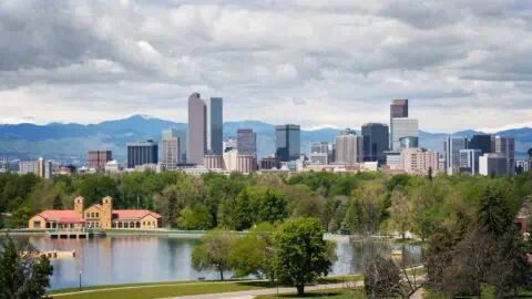 a view of downtown denver's skyline, a lake and park can be seen in the foreground