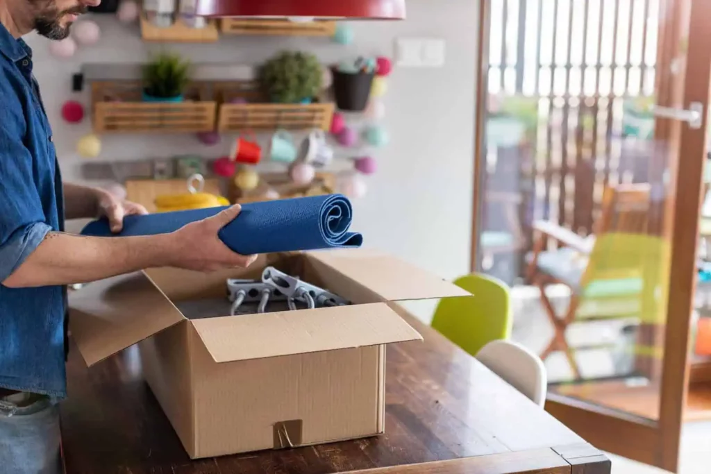 A man places a yoga mat into a box filled with other small and light pieces of exercise equipment, like bands 