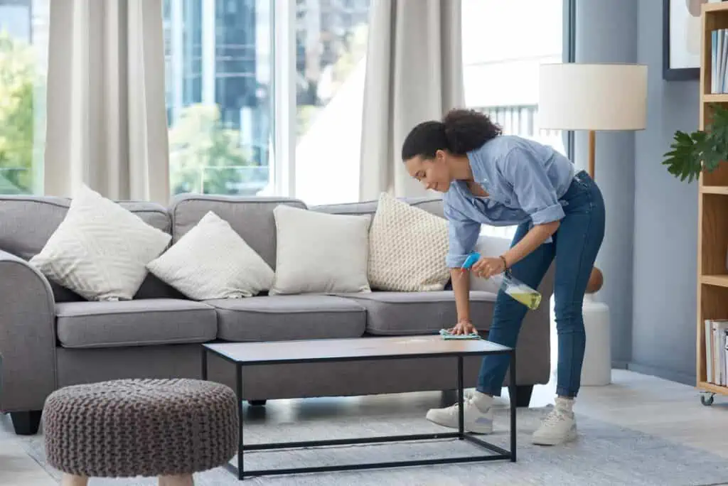 a woman dusts off a table in a living room in preparation for a real estate photo