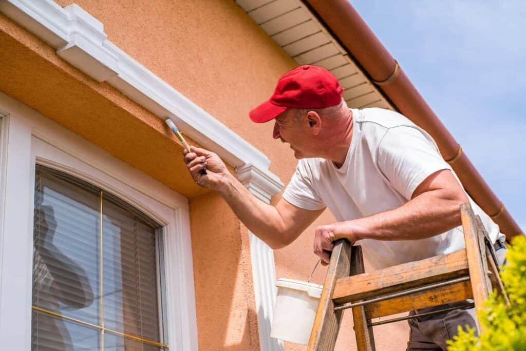 a man on a ladder paints a windowsill 