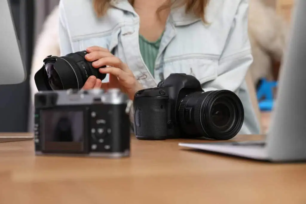 a woman looks over different types of cameras and lenses on the table in front of her