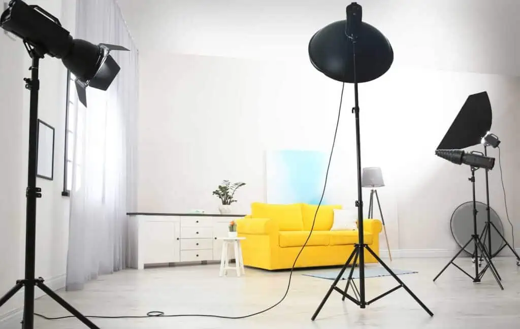 photography lighting equipment shines light around a yellow couch and dresser in preparation for a photo to be taken of the furniture
