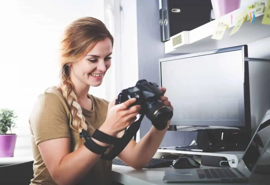 a woman looks at images on a professional digital camera seated at a desk with a large monitor