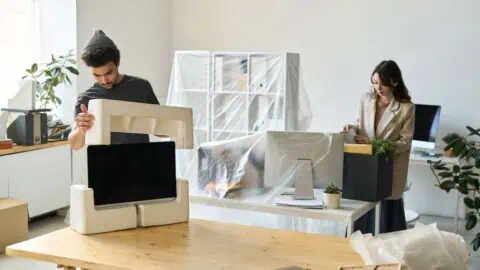 two employees packing up computer monitors and furniture for their office's move
