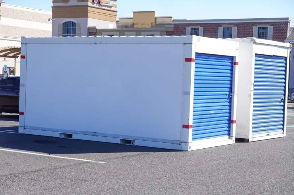 two white moving storage containers with blue doors sit on an asphalt surface 