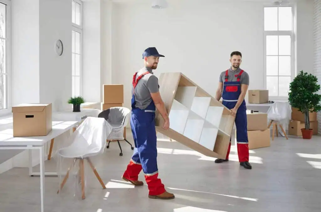 two movers dressed in overalls move a shelf from an office