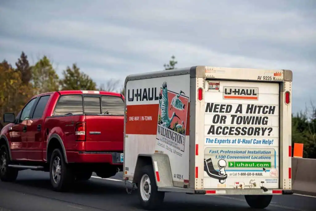A red truck tows a uhaul trailer down a highway