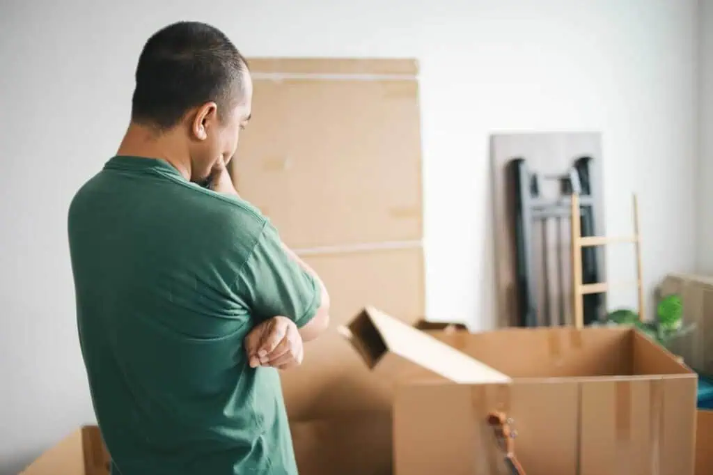 A man looks contemplative as he stares at boxes stacked in a room