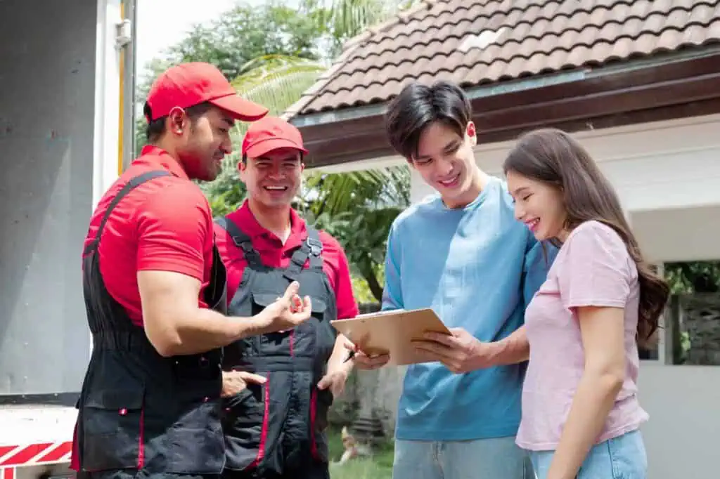 A couple talks to movers and looks over a clipboard with cost and term agreements