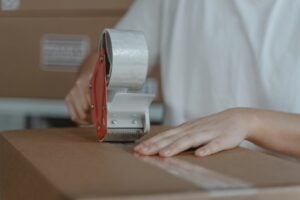 A person is closing a packing box with a tape dispenser 
