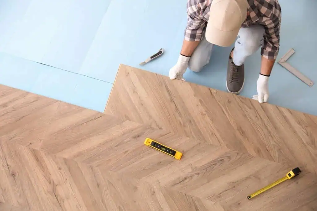 A person installs laminate flooring with a herringbone wood pattern