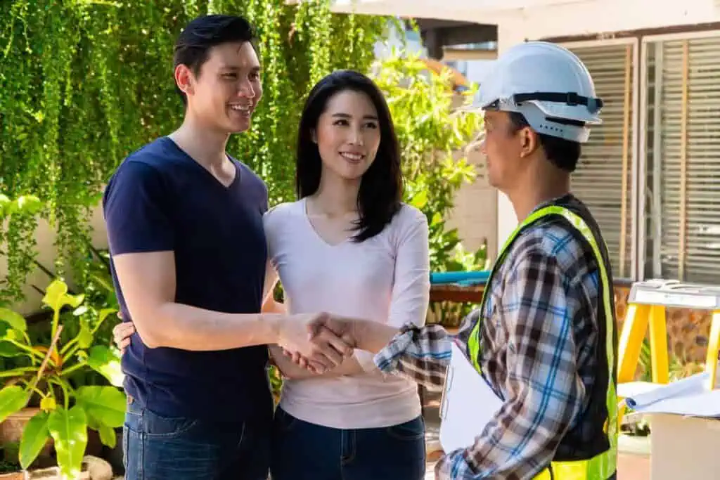 A couple talks and shakes hands with a contractor in a hardhat and reflective vest