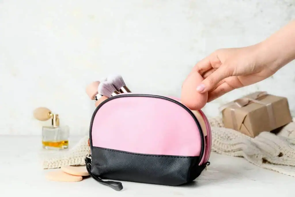 someone puts a pink makeup sponge into a bag filled with makeup brushes