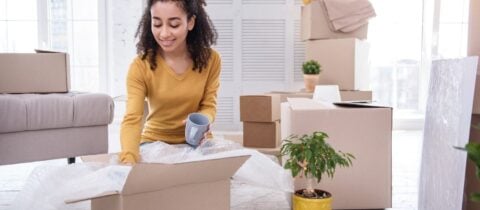 A woman packs mugs into.a boxes filled with bubble wrap