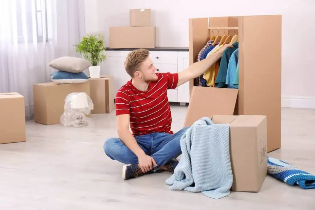 A man sits on the floor of his living room and looks through the contents of a wardrobe box