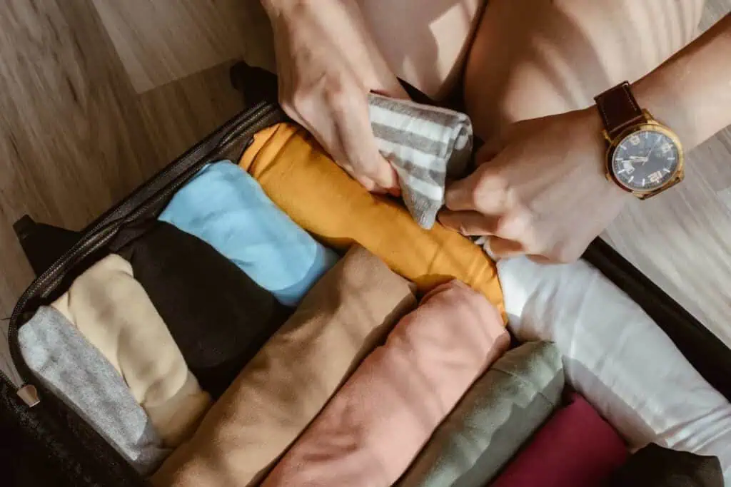 Someone adds a rolled up t-shirt to a suitcase already packed with other rolled up clothing