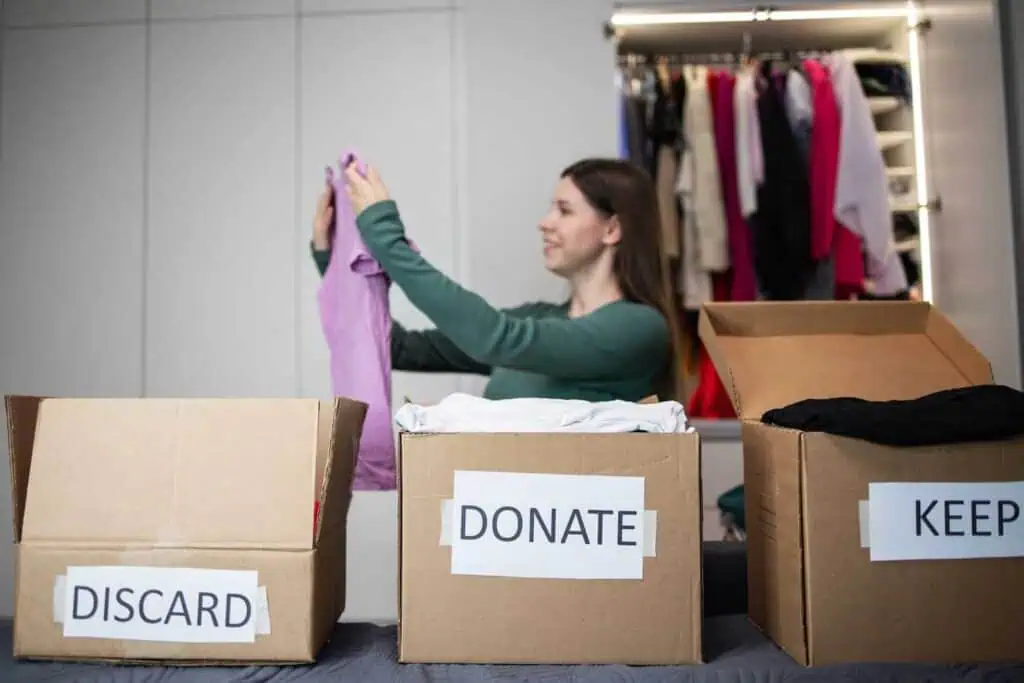 A woman organizes clothing into three boxes labeled discard, donate, and keep in order from left to right