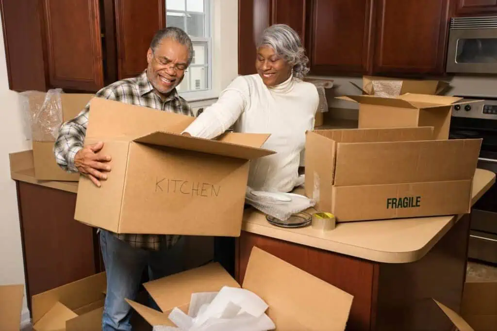 A couple happily unpacks a box labeled "kitchen" in their new home