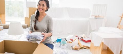 a young woman smiles as she packs dishes into a box