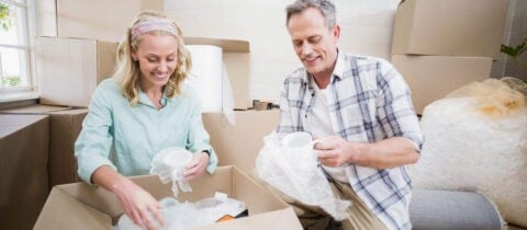A couple wraps mugs and glasses in bubble wrap to put into a box