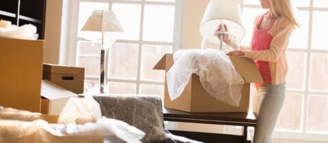 A woman puts a white lamp into a box with bubble wrap