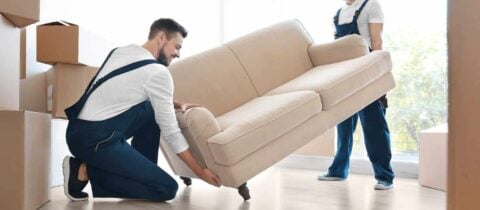 two movers work together to lift a white couch