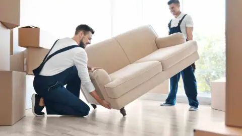 two movers work together to lift a white couch