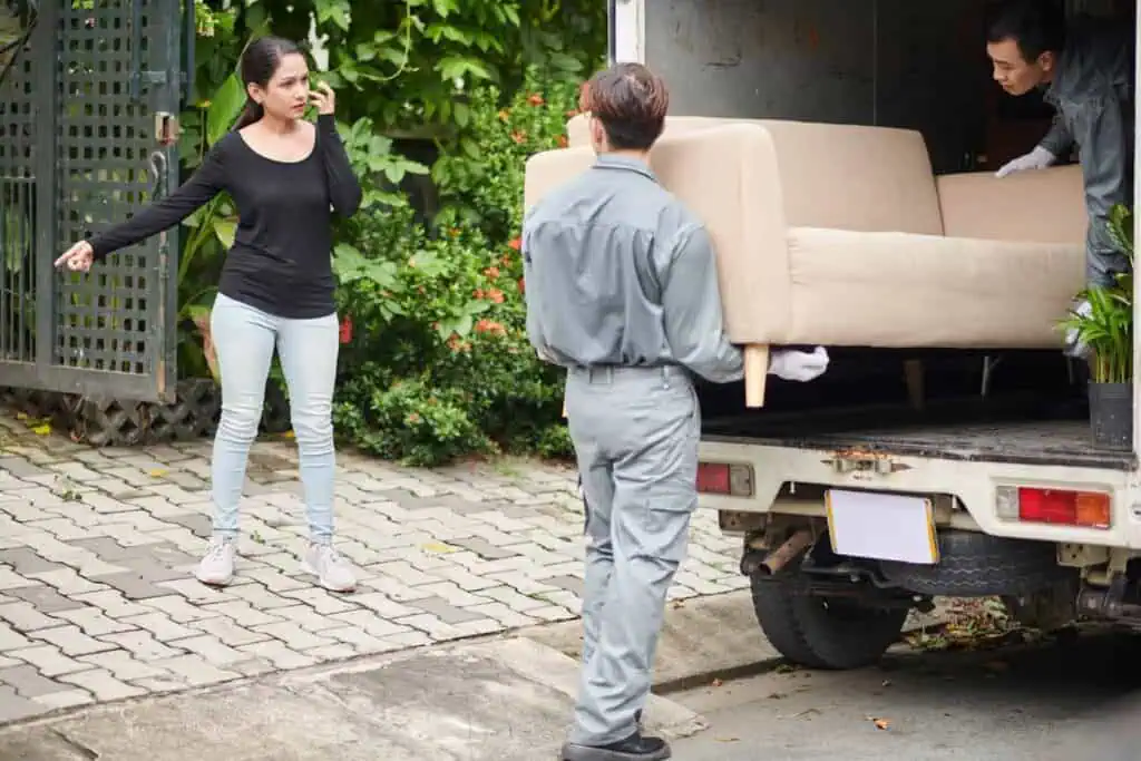A woman directs who movers where to take a couch they're unloading from a truck