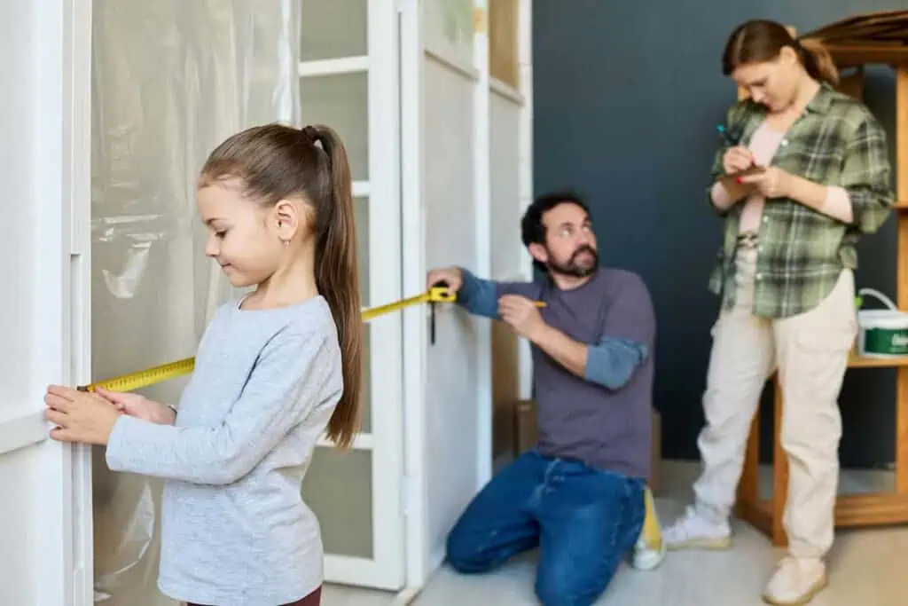 A young girl helps her parents measure the width of a doorway