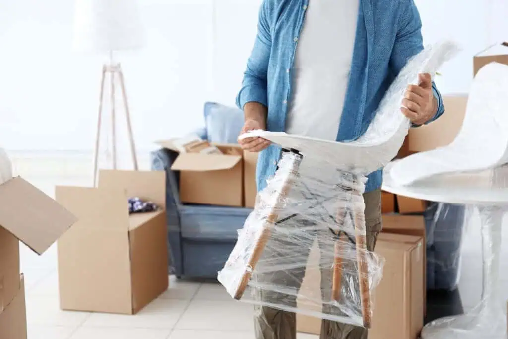 A man carries a white chair that has been shrink-wrapped for protection