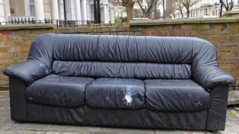 an old black couch is sitting at the curb