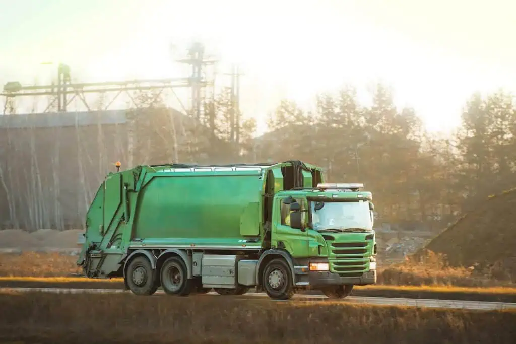 a municipal garbage truck drives down a road in the early morning