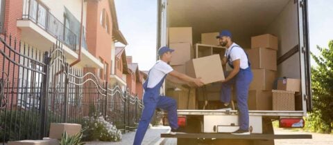 Two movers in blue overalls unload a full truck