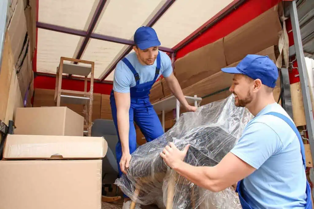 two movers unload a wrapped chair from a truck full of other furniture