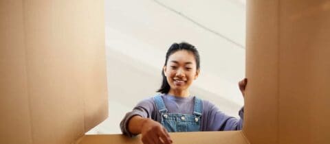 A woman sets down an item into a box. The angle of the shot is from the bottom of the box pointing upwards, so it looks as through the woman is reaching towards the camera