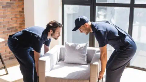 two movers work to lift a upholstered chair