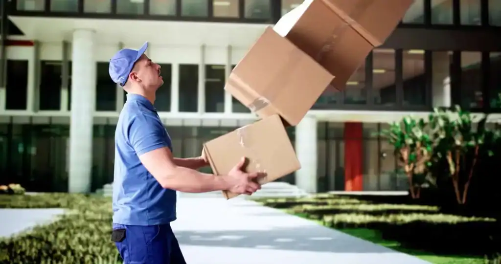 Mover dropping cardboard boxes during a house move outside a building.