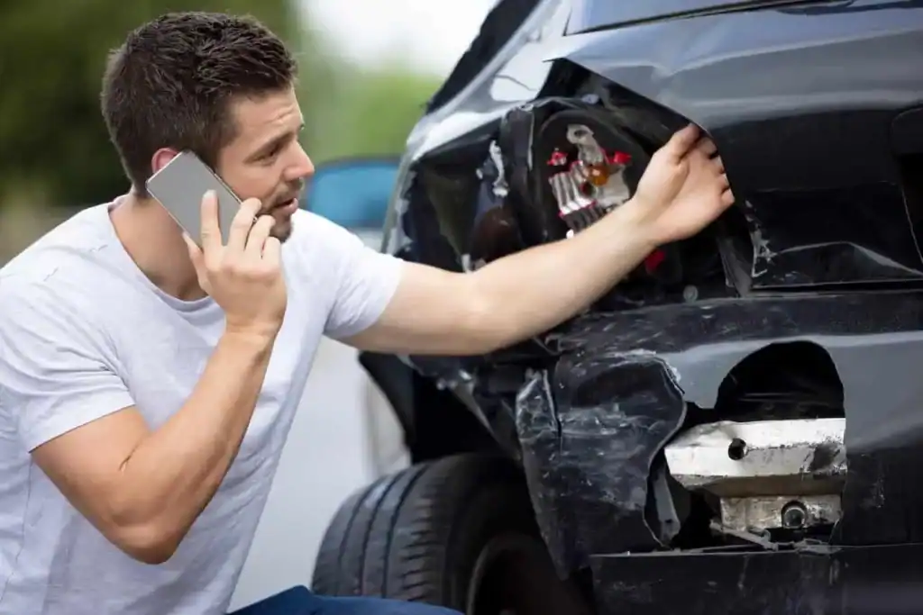 Man calling insurance after a car accident with visible damage.