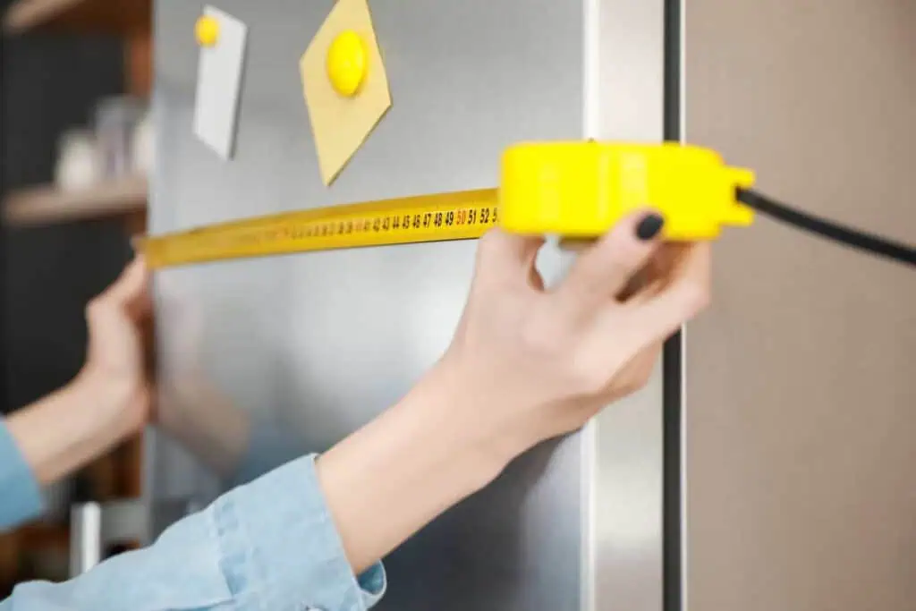 someone measures the width of their fridge with yellow measuring tape